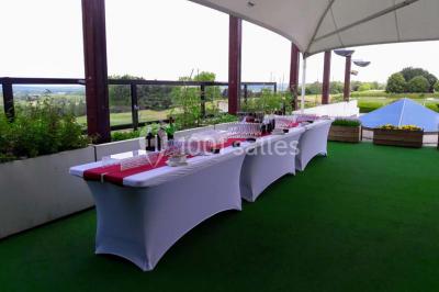 Salle de réception décorée avec des tables rondes, nappes blanches et chaises ornées de nœuds colorés.
