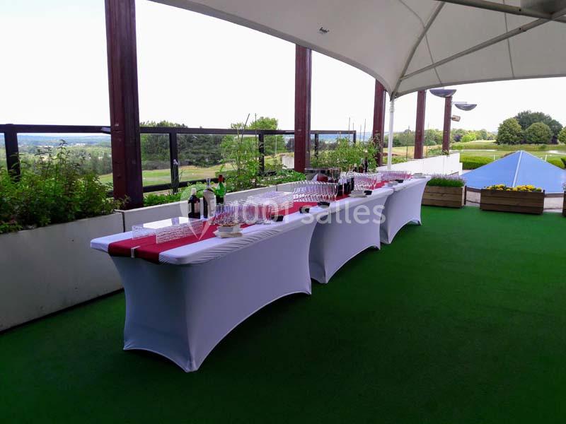 Tables dressées avec nappes blanches, verres et bouteilles, sous une structure couverte avec vue sur un espace extérieur…