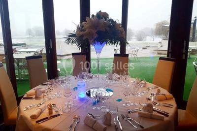 Salle de réception décorée avec des tables rondes, nappes blanches et chaises ornées de nœuds colorés.