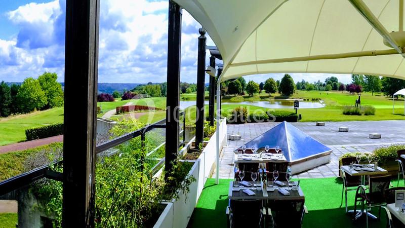 Terrasse couverte avec vue sur un parcours de golf, des tables dressées et un paysage verdoyant en arrière-plan.