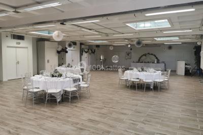 Salle de réception décorée avec des tables rondes, nappes blanches et chaises ornées de nœuds colorés.