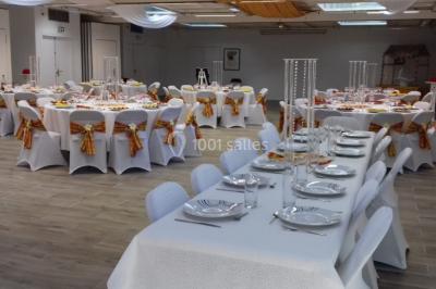 Salle de réception décorée avec des tables rondes, nappes blanches et chaises ornées de nœuds colorés.
