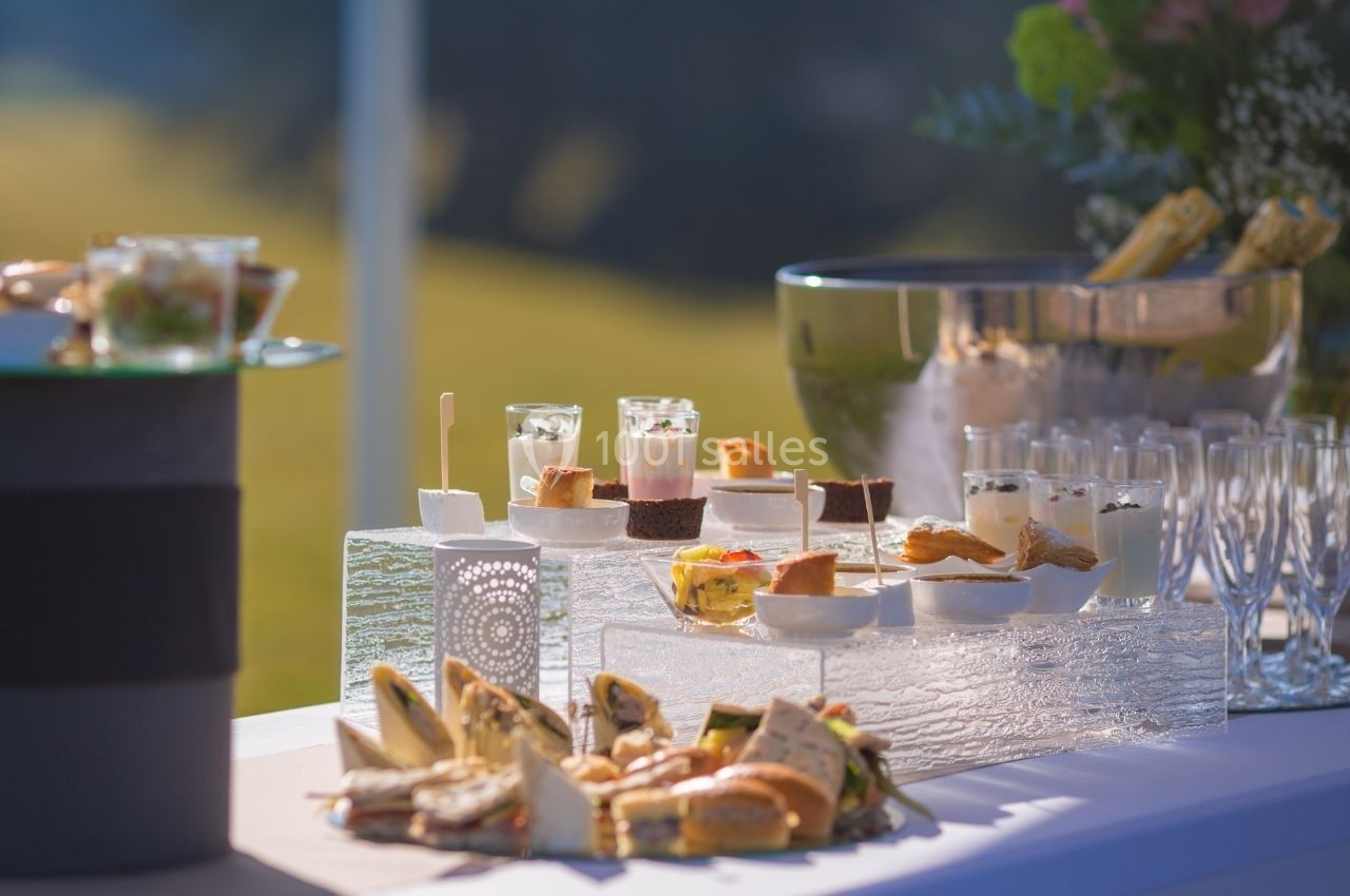 Table dressée avec des amuse-bouches variés, des desserts et des verres, dans un cadre extérieur ensoleillé.