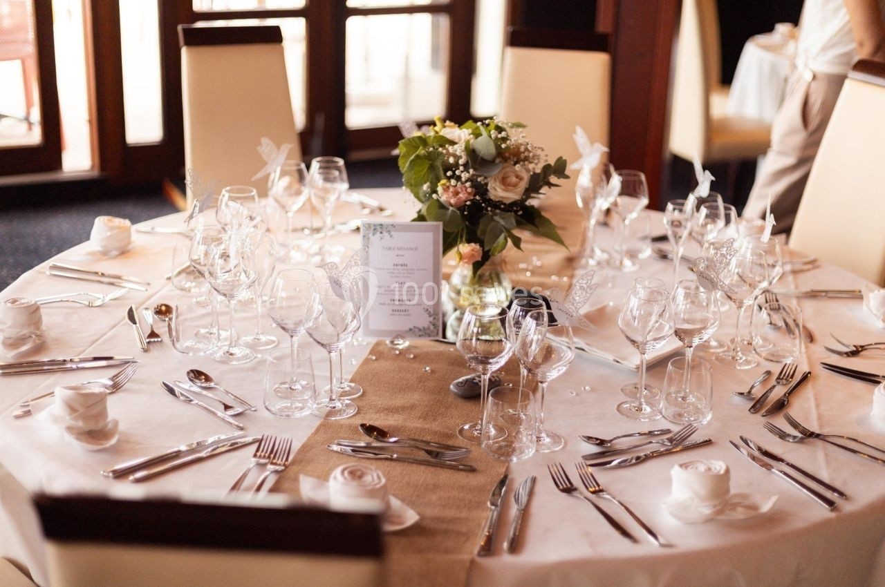 Table ronde élégamment dressée avec nappes blanches, vaisselle raffinée, verres et centre de table floral.