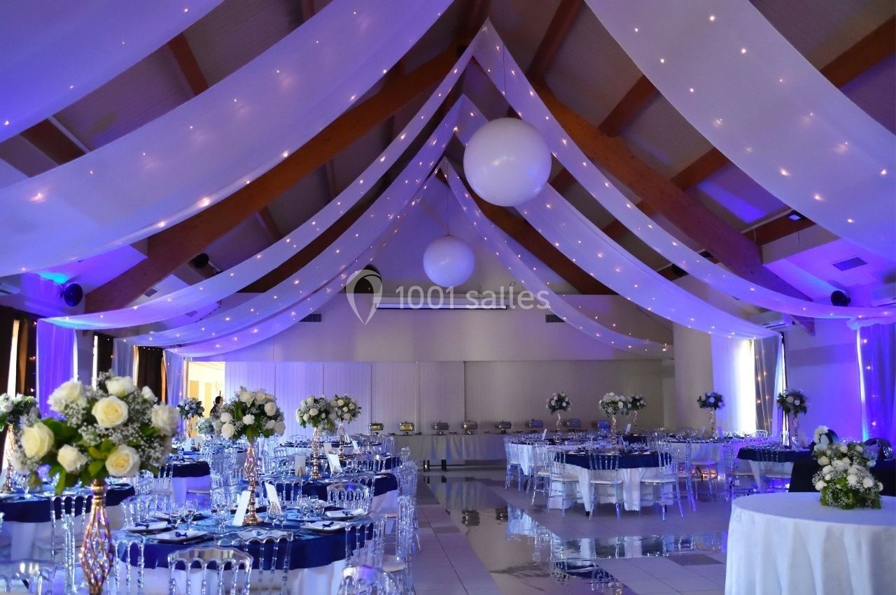 Salle de réception décorée avec des guirlandes lumineuses, des tables dressées et des arrangements floraux élégants.