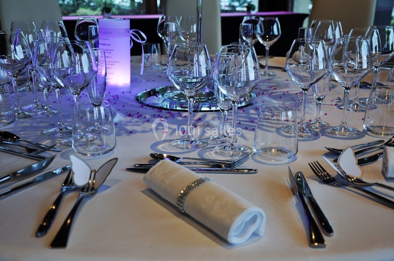 Table dressée pour un événement avec nappes blanches, verres, couverts, serviettes pliées et décoration élégante.
