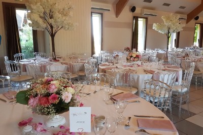 Salle lumineuse avec tables rondes dressées, nappes blanches, chaises rouges et décorations florales élégantes.