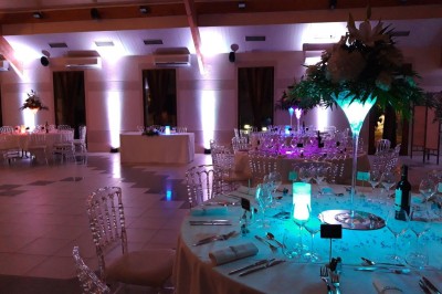 Salle lumineuse avec tables rondes dressées, nappes blanches, chaises rouges et décorations florales élégantes.