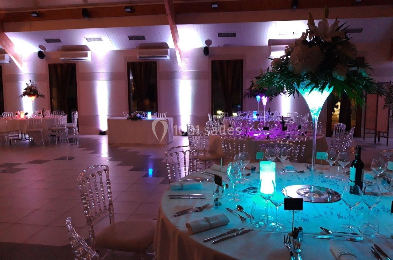 Salle de réception décorée avec des tables élégantes, des chaises transparentes et un éclairage d'ambiance coloré.