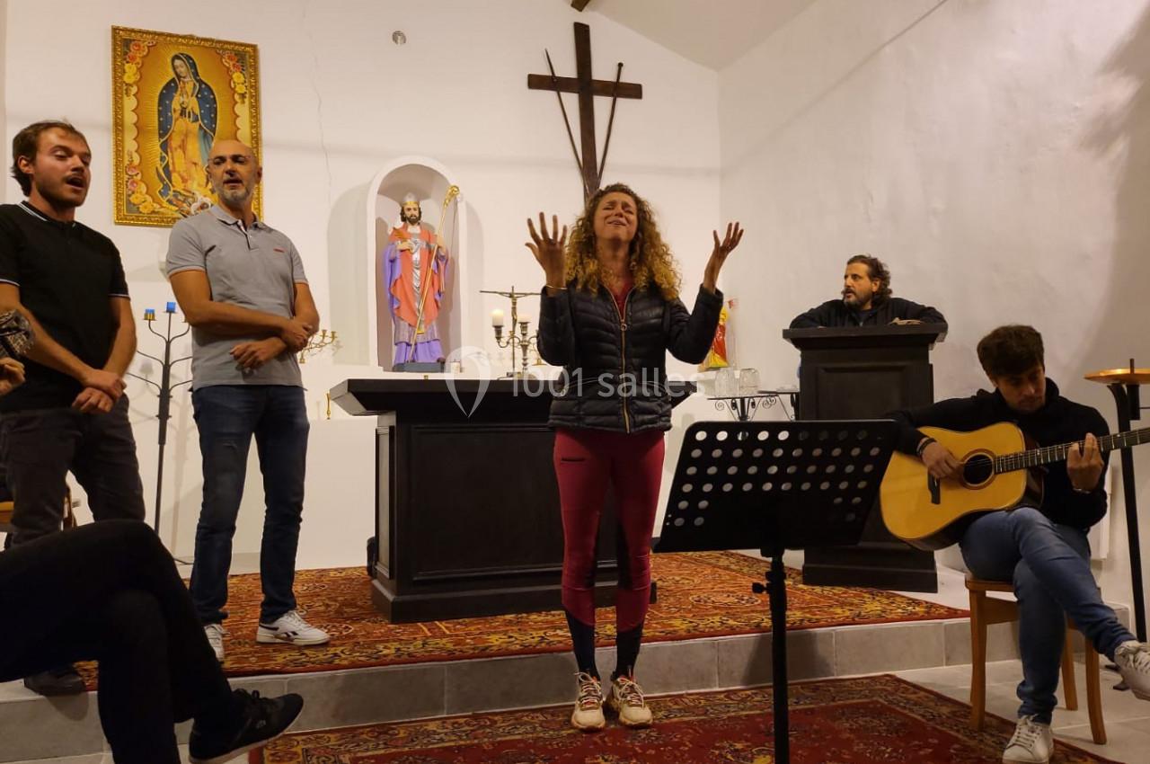 Un groupe de personnes chante et joue de la musique dans une petite chapelle avec un autel en arrière-plan.