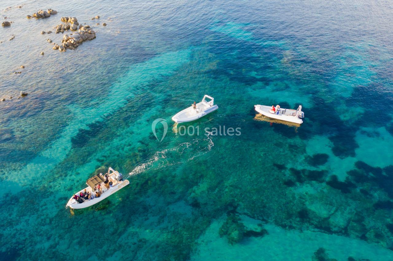 Trois bateaux à moteur naviguent sur une eau turquoise et claire, entourés de rochers immergés.