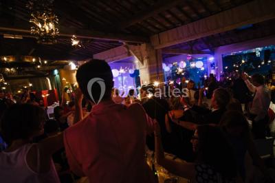 Salle en pierre avec arches, tables décorées et stands alignés, éclairage chaleureux créant une ambiance conviviale.