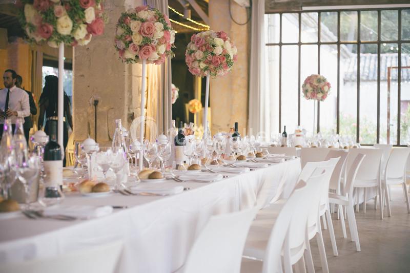 Salle de réception décorée avec des tables dressées, nappes blanches, bouquets de fleurs et lumière naturelle.