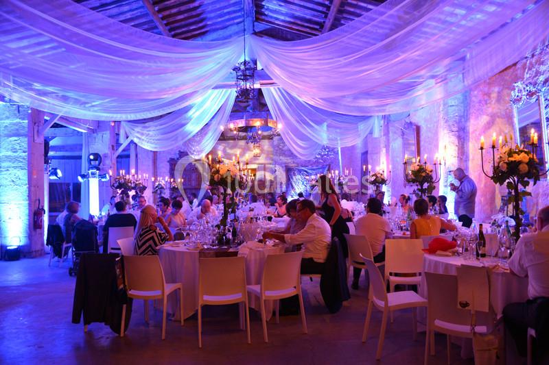 Salle de réception décorée avec des voilages blancs et éclairages colorés, tables dressées pour un dîner festif.