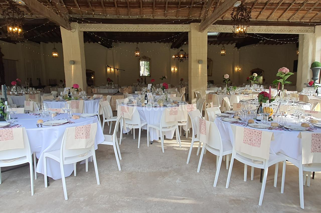 Salle de réception décorée avec des tables rondes dressées, nappes blanches et fleurs colorées.