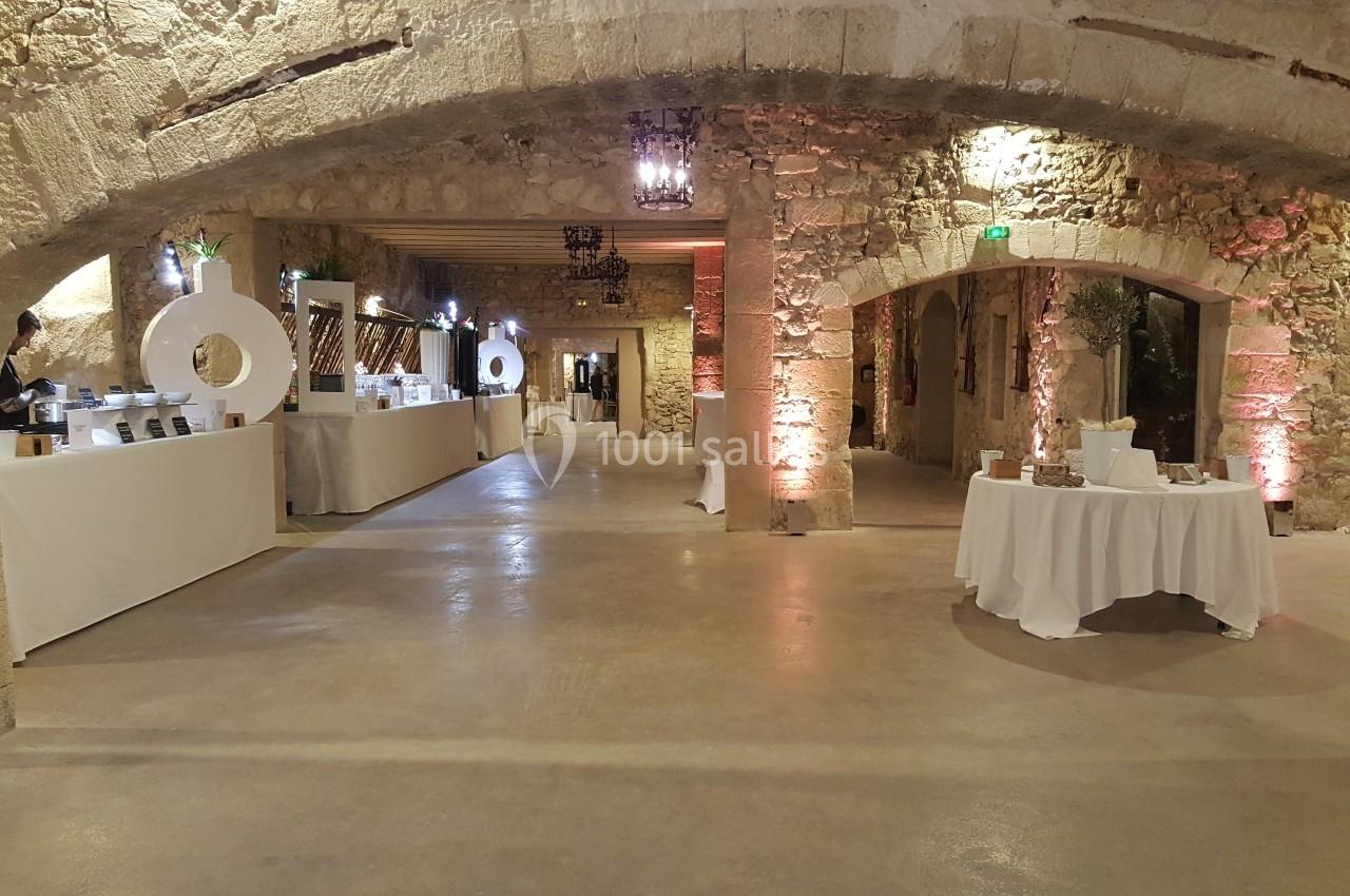 Salle en pierre avec arches, tables décorées et stands alignés, éclairage chaleureux créant une ambiance conviviale.