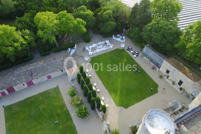 Cour d'une maison en pierre avec façade recouverte de lierre, arbres en arrière-plan et ciel bleu dégagé.