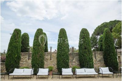 Cour d'une maison en pierre avec façade recouverte de lierre, arbres en arrière-plan et ciel bleu dégagé.
