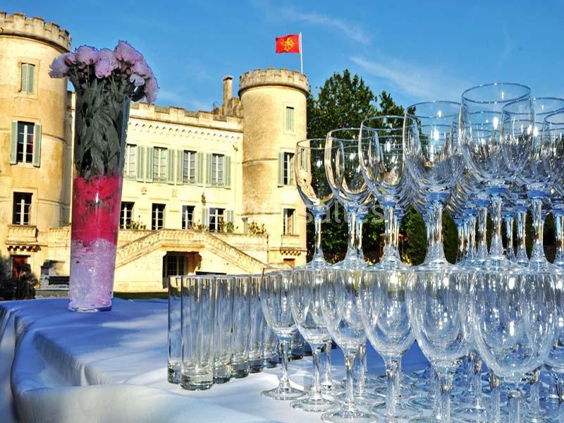 Verres en cristal disposés sur une table blanche devant un château avec une tour ornée d'un drapeau rouge.