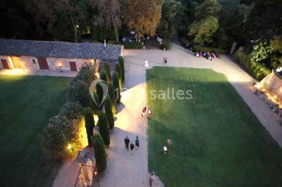 Cour d'une maison en pierre avec façade recouverte de lierre, arbres en arrière-plan et ciel bleu dégagé.