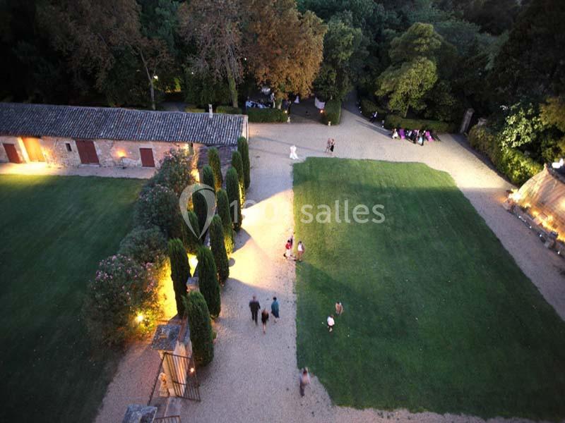 Vue aérienne d'une cour avec pelouse, allées gravillonnées, arbres, bâtiments en pierre et éclairage nocturne.