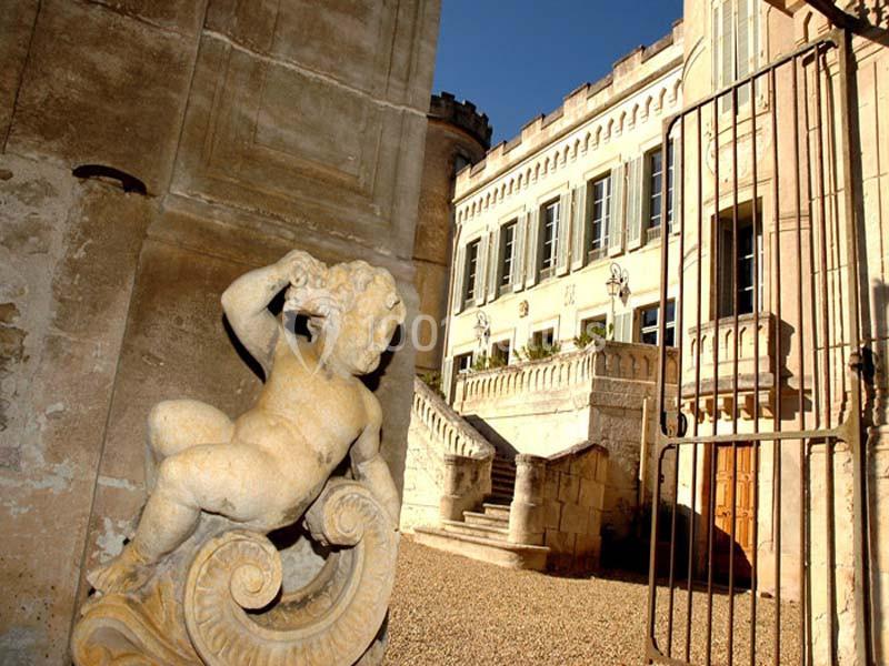 Statue en pierre d'un ange devant un bâtiment historique avec façade ornée et portail en fer forgé.