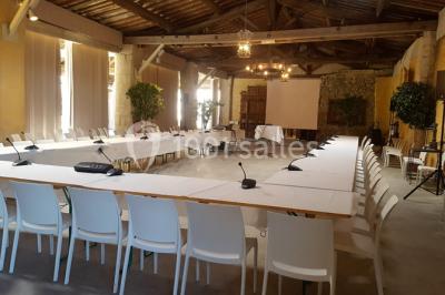 Cour d'une maison en pierre avec façade recouverte de lierre, arbres en arrière-plan et ciel bleu dégagé.
