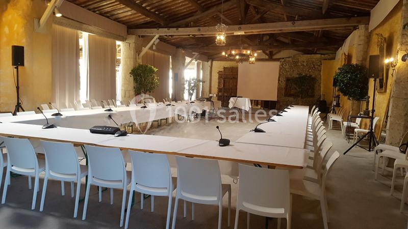 Salle de réunion lumineuse avec une grande table en U, chaises blanches, micros et projecteur.