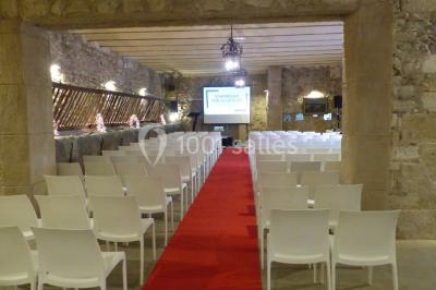 Cour d'une maison en pierre avec façade recouverte de lierre, arbres en arrière-plan et ciel bleu dégagé.