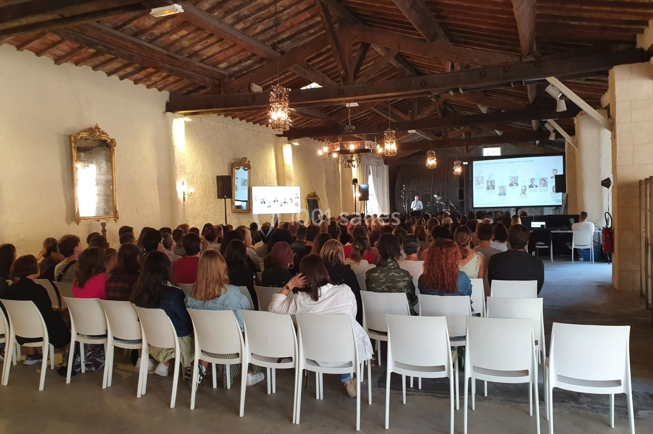 Un groupe de personnes assises dans une salle avec un plafond en bois, assistant à une présentation sur écran.