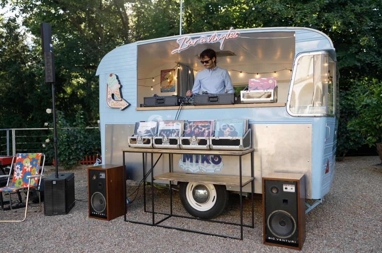 Un DJ mixe de la musique dans une caravane aménagée, entourée de vinyles et d'équipements audio en extérieur.