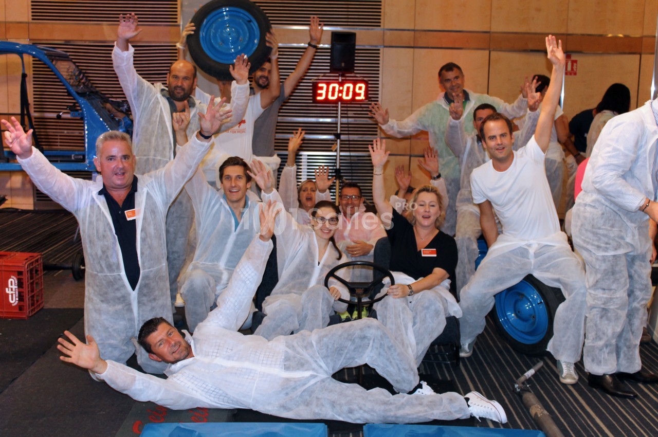 Un groupe de personnes en combinaisons blanches pose joyeusement devant un chronomètre dans un cadre intérieur.