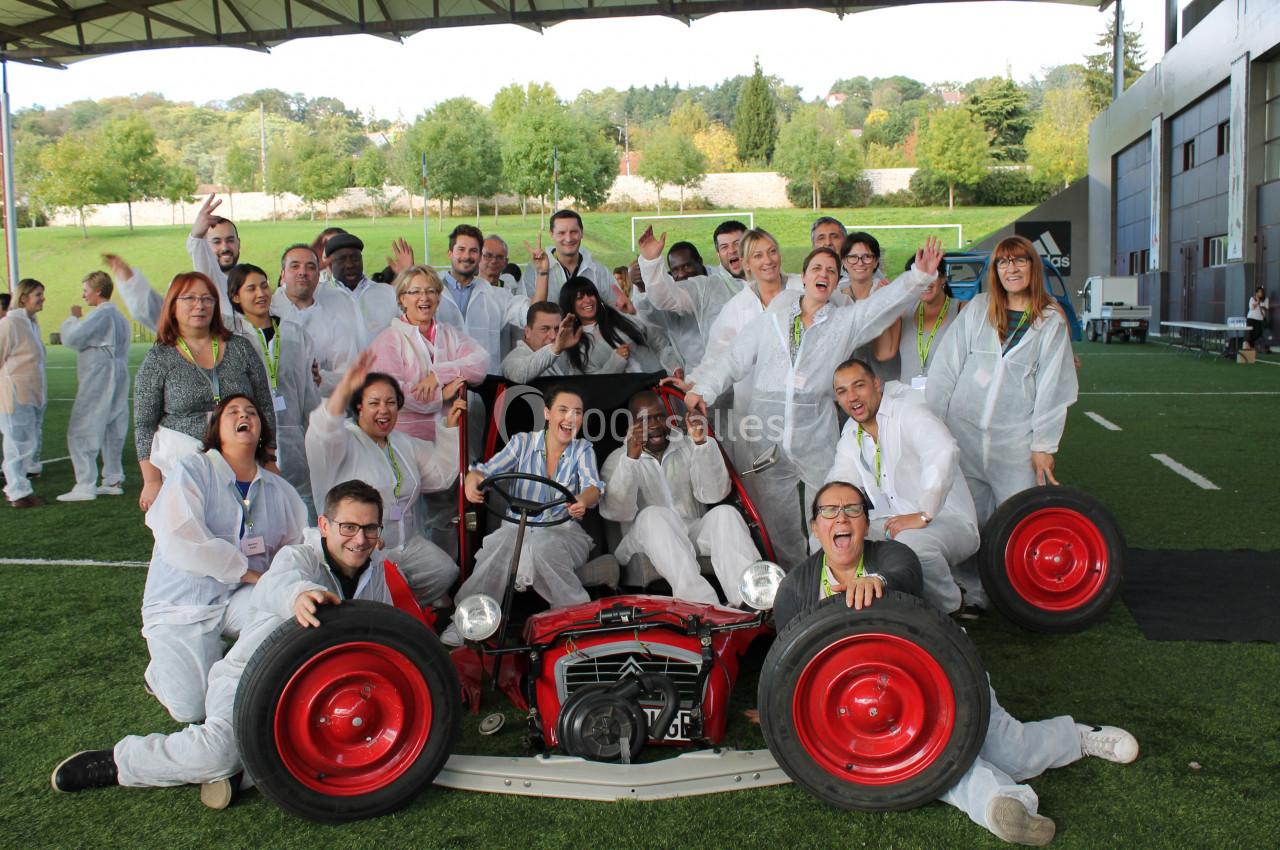 Un groupe de personnes souriantes posant autour d'un ancien tracteur rouge sur une pelouse.