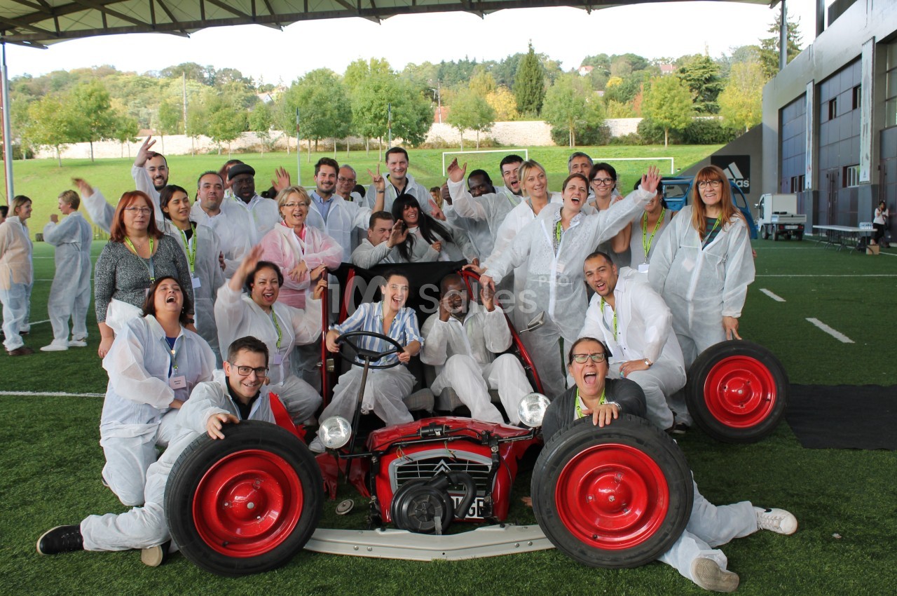 Un groupe de personnes souriantes posant autour d'un ancien tracteur rouge sur une pelouse.