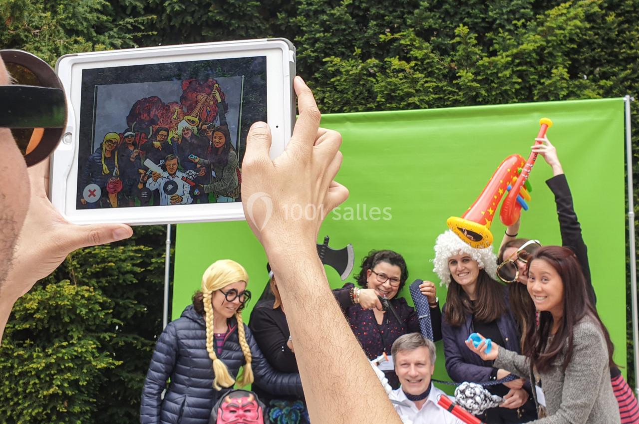 Un groupe de personnes déguisées pose devant un fond vert, photographié à travers une tablette tenue par une autre personne.