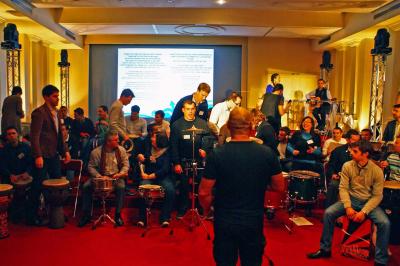 Des personnes debout en cercle dans une grande salle colorée, participant à une activité collective.