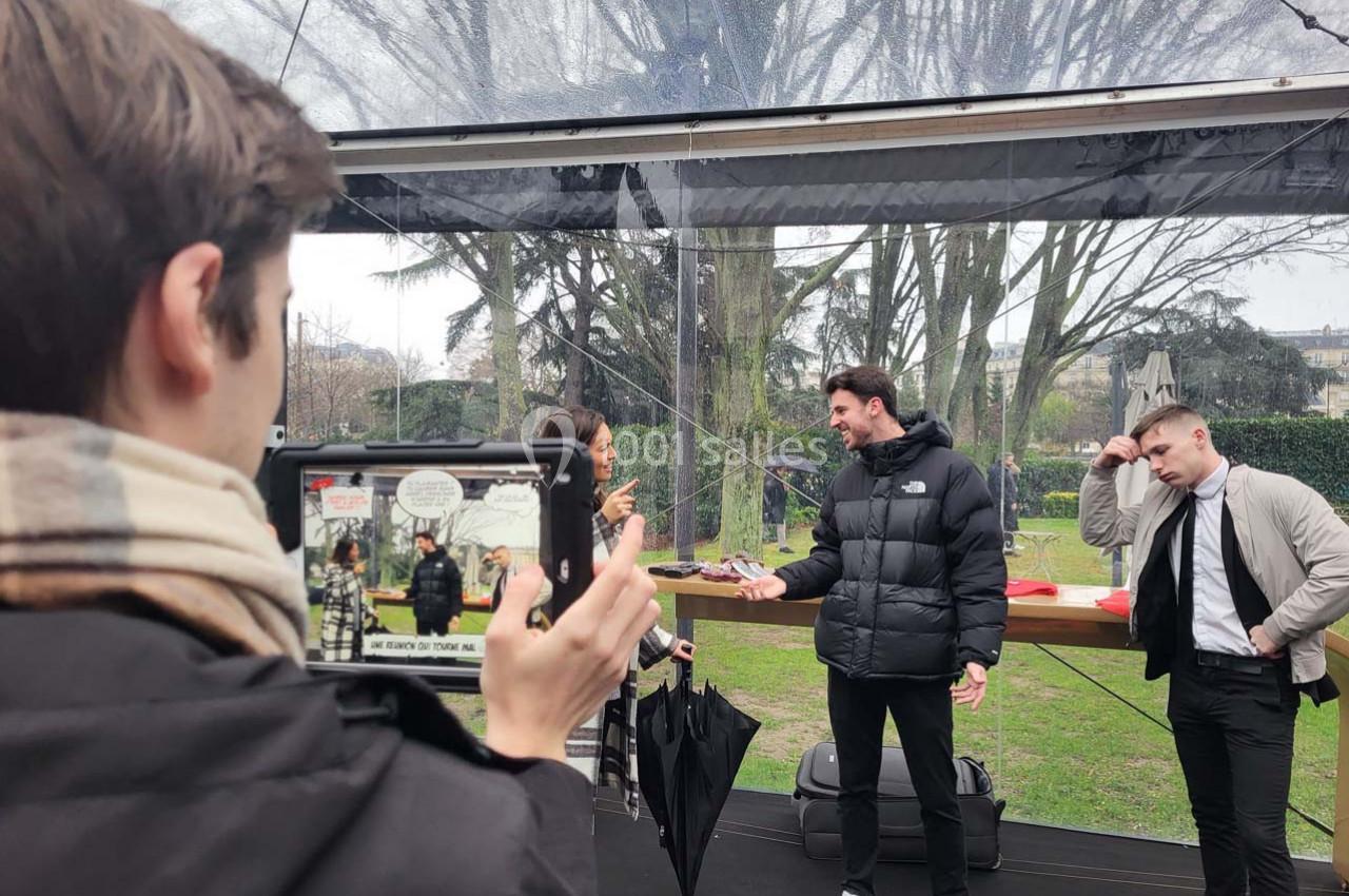 Un homme est filmé avec une tablette tandis qu'il discute avec deux autres personnes sous une structure transparente.