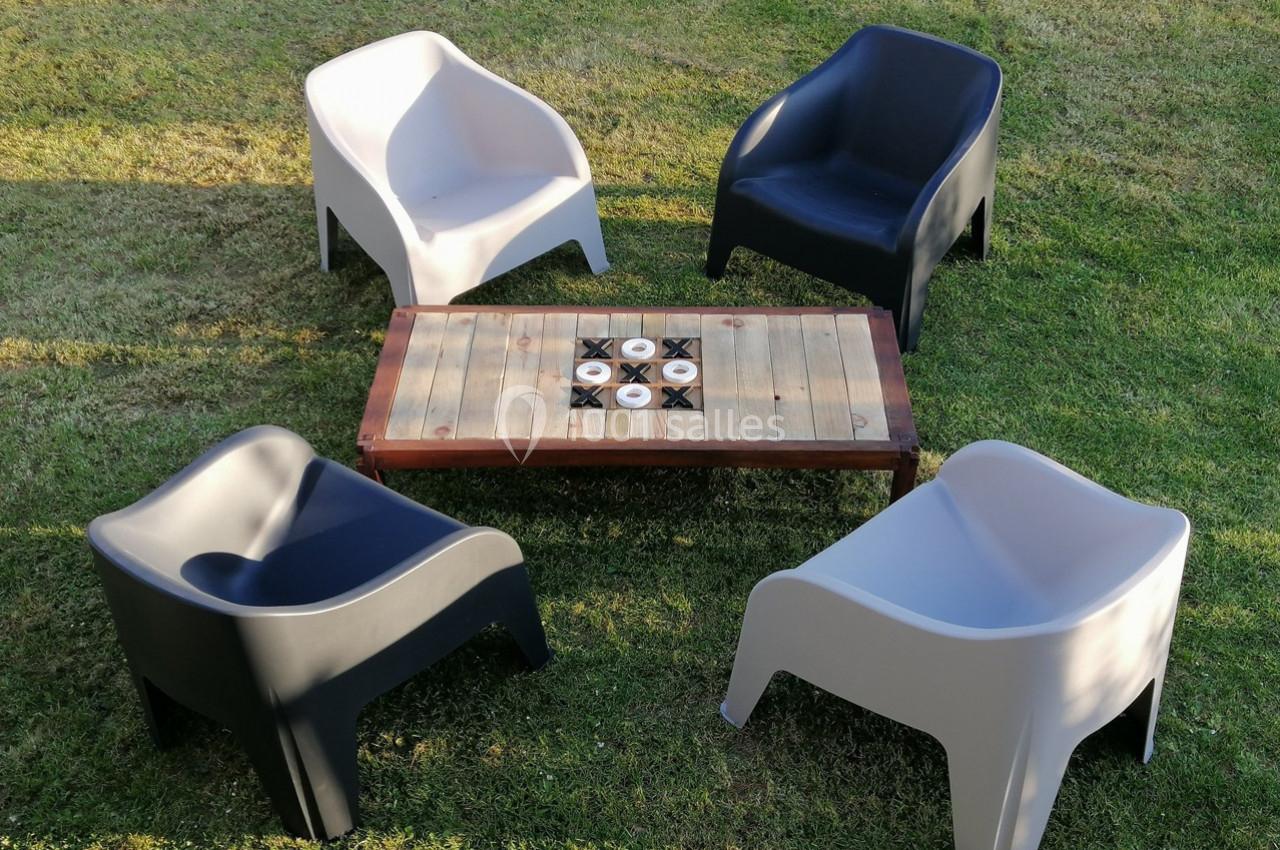 Quatre fauteuils en plastique, deux noirs et deux blancs, entourent une table basse en bois sur une pelouse.