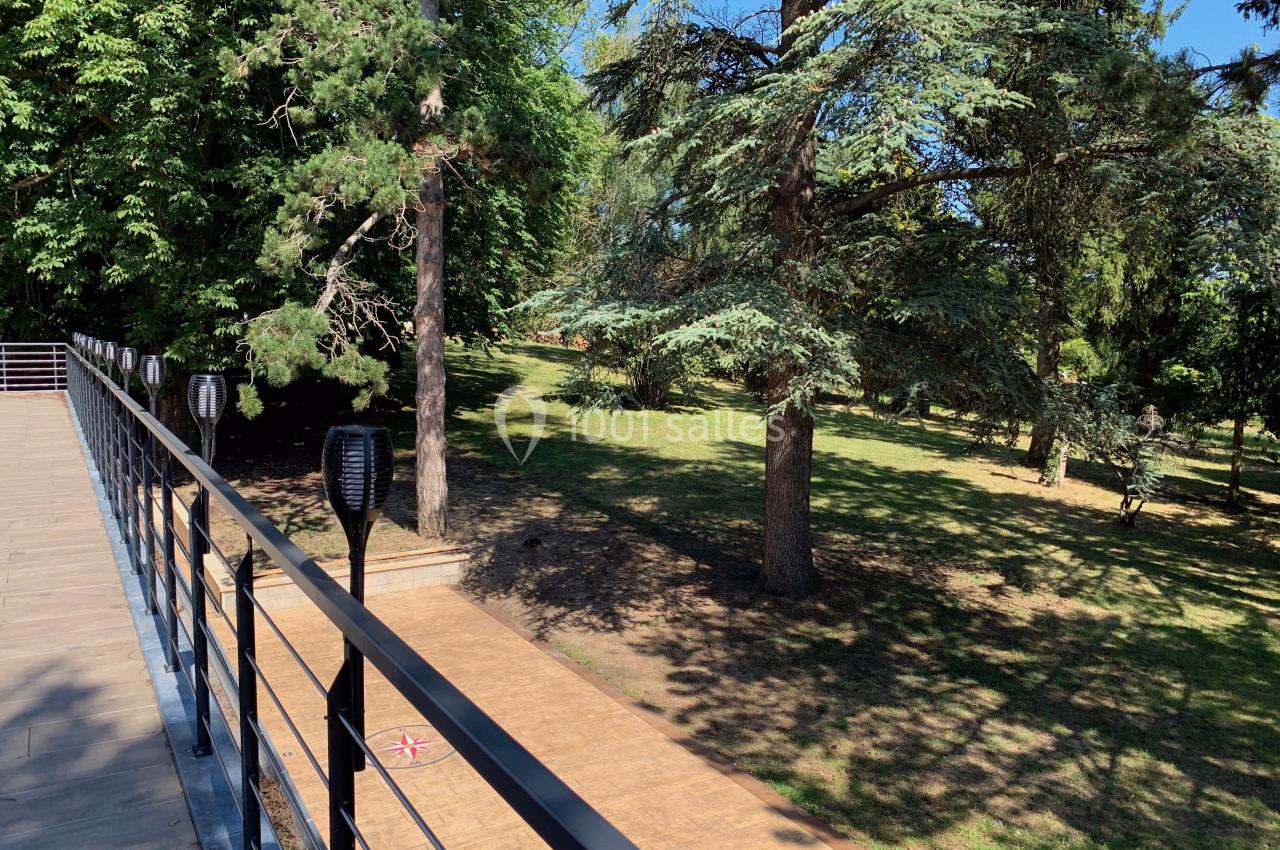 Location salle Monceaux (Oise) - Domaine de Monceaux #12 Passerelle en bois bordée de lampadaires, surplombant un parc arboré baigné de lumière naturelle.