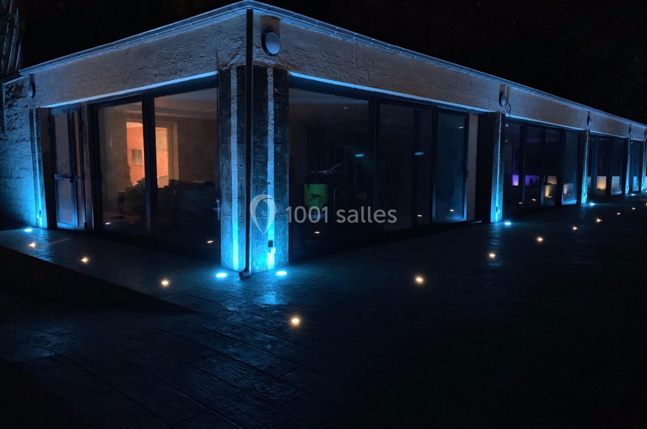 Location salle Monceaux (Oise) - Domaine de Monceaux #14 Façade vitrée d'un bâtiment moderne éclairée par des lumières bleues et des spots encastrés au sol, de nuit.
