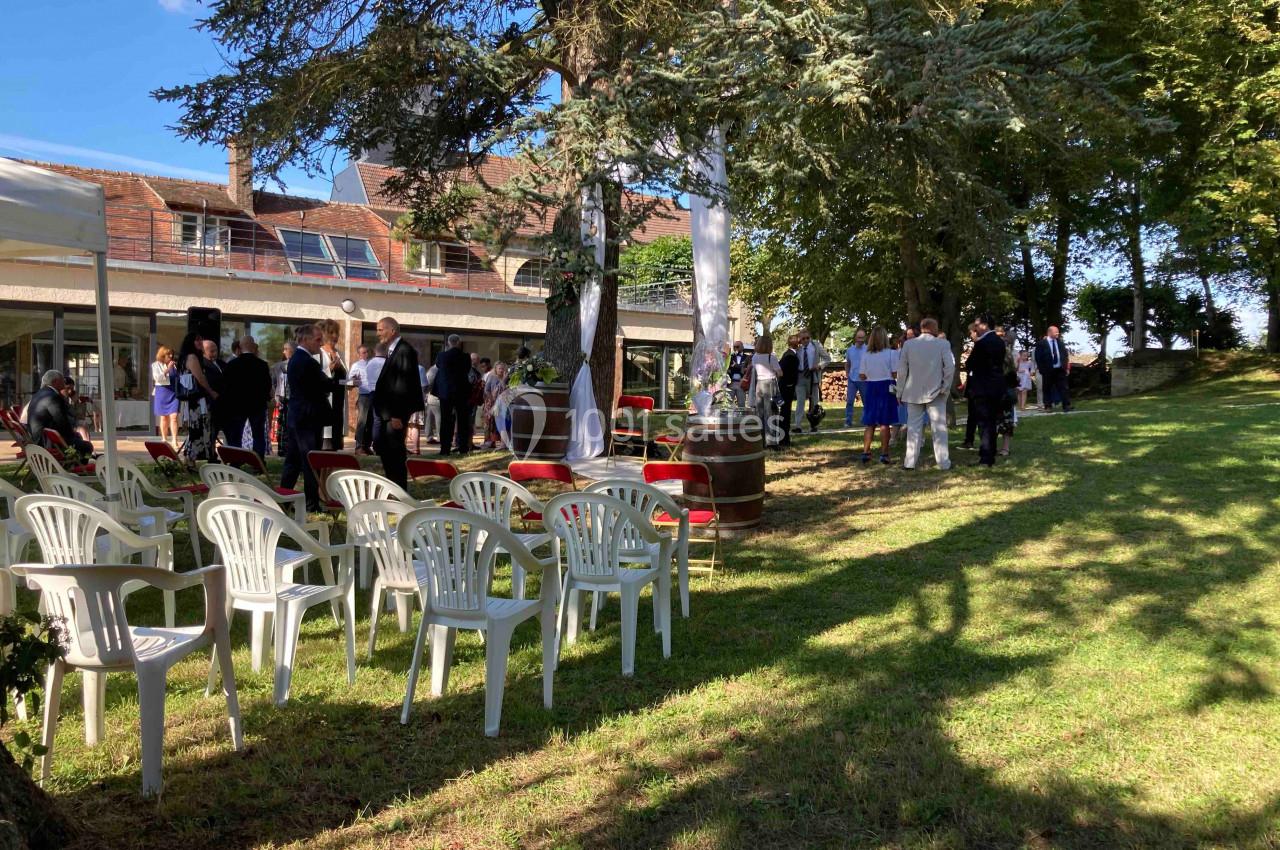 Location salle Monceaux (Oise) - Domaine de Monceaux #17 Des personnes rassemblées dans un jardin ombragé avec des chaises en plastique blanc et un bâtiment en arrière-plan.