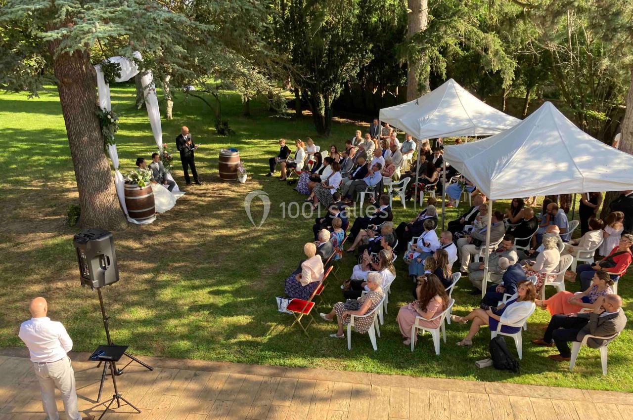 Location salle Monceaux (Oise) - Domaine de Monceaux #19 Cérémonie en plein air avec des invités assis sous des arbres et des tentes blanches dans un cadre verdoyant.