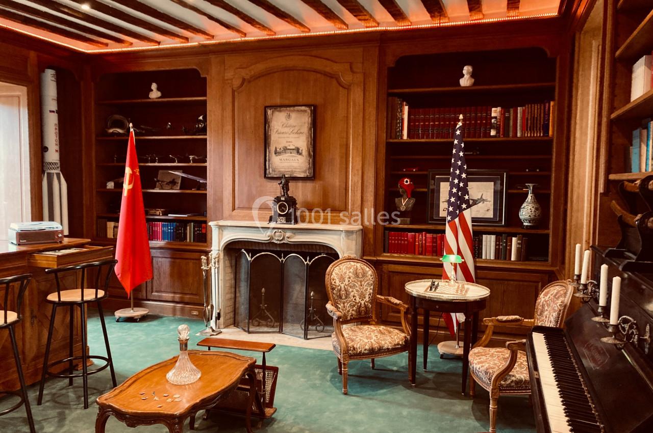 Location salle Monceaux (Oise) - Domaine de Monceaux #4 Bibliothèque avec cheminée, drapeaux chinois et américain, piano, fauteuils anciens et étagères remplies de livres.