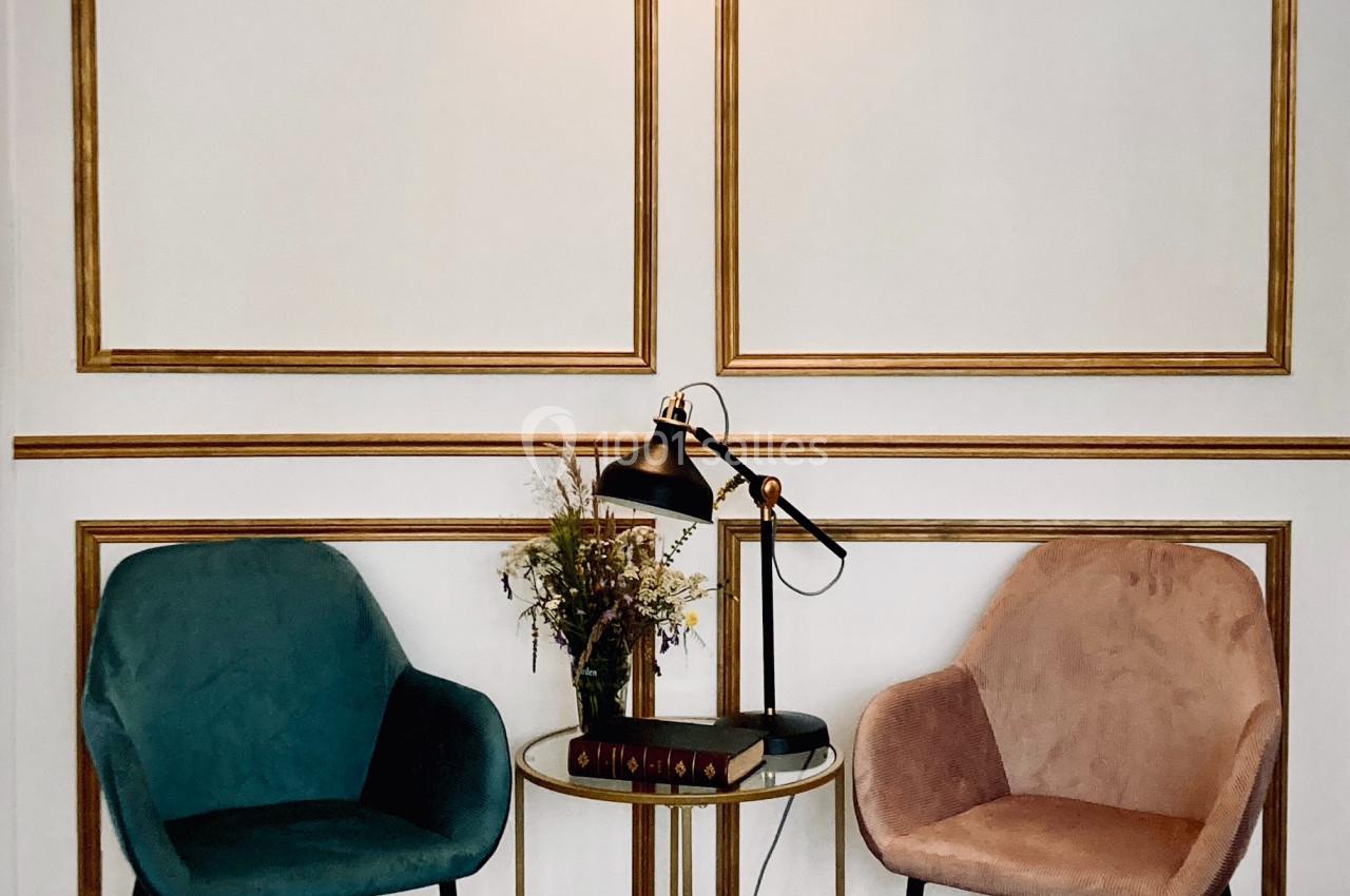 Location salle Monceaux (Oise) - Domaine de Monceaux #22 Deux fauteuils colorés entourent une table ronde avec une lampe, des livres et un bouquet, sur un sol en damier.