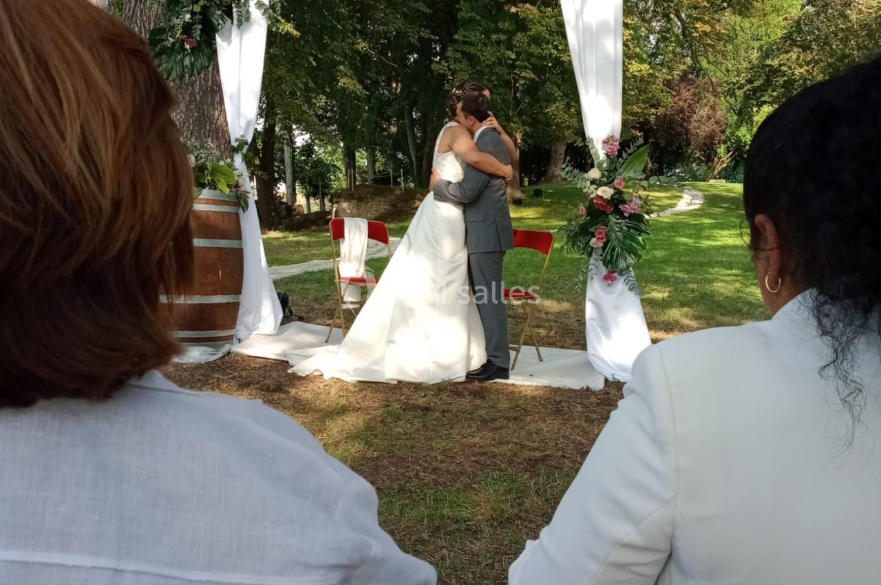Location salle Monceaux (Oise) - Domaine de Monceaux #6 Un couple s'embrasse sous une arche décorée de fleurs lors d'une cérémonie de mariage en plein air.