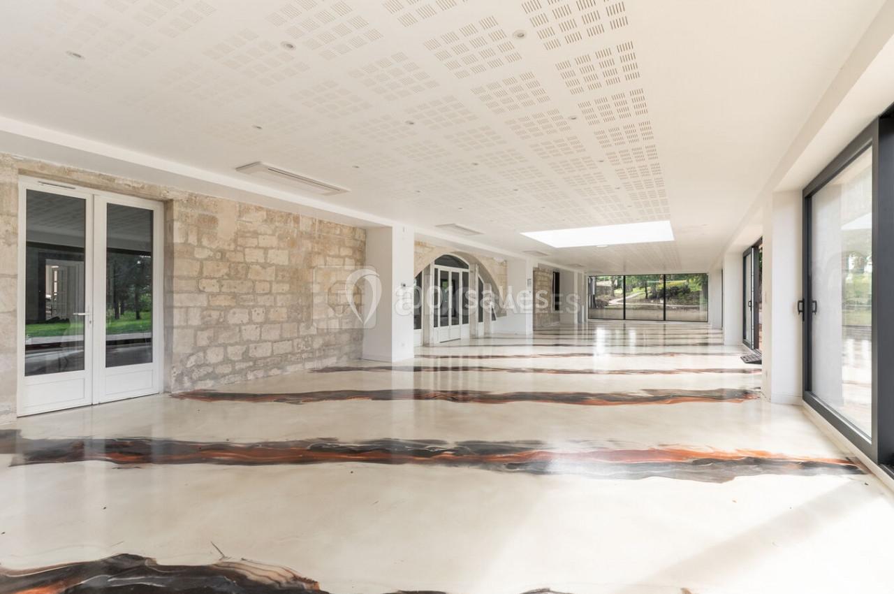 Location salle Monceaux (Oise) - Domaine de Monceaux #5 Salle lumineuse avec sol en résine aux motifs organiques, murs en pierre et grandes baies vitrées donnant sur un jardin.