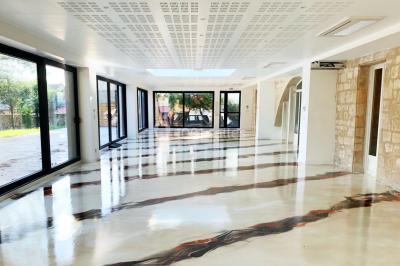 Salle avec un sol en damier noir et beige, cheminée en bois, murs blancs et grandes fenêtres cintrées.