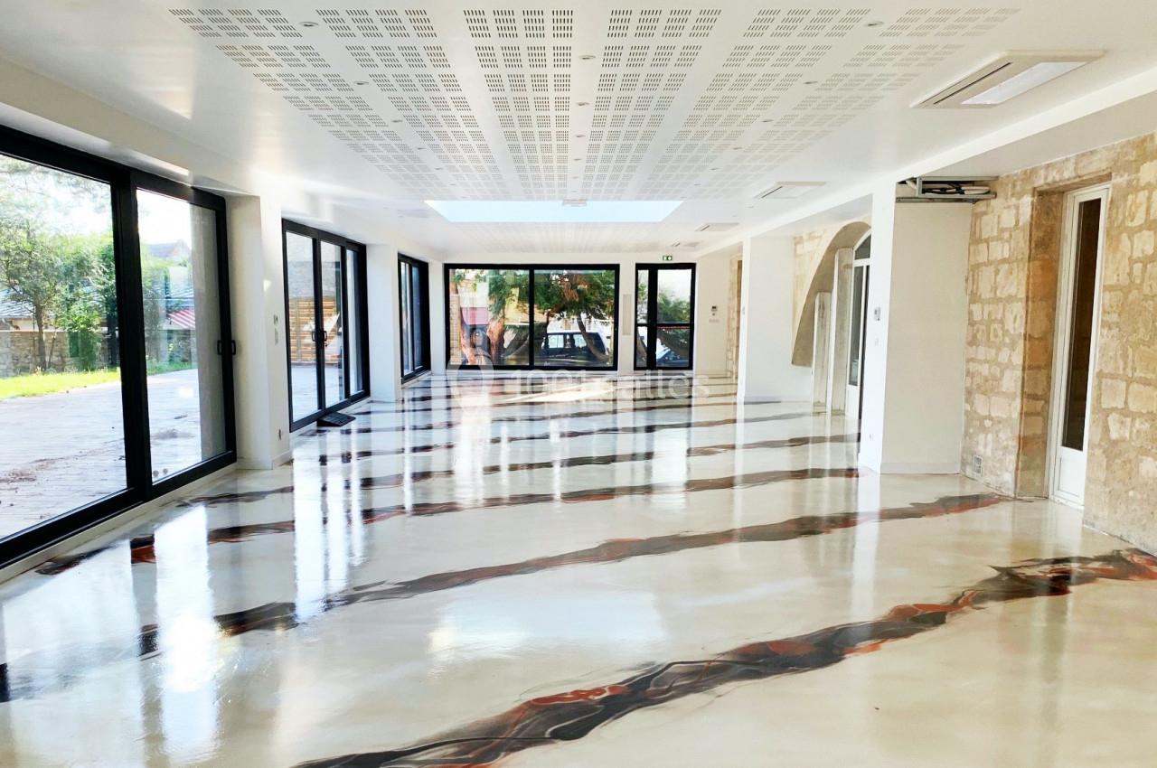 Salle lumineuse avec de grandes baies vitrées, murs en pierre et sol en résine aux motifs abstraits.