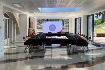 Salle avec un sol en damier noir et beige, cheminée en bois, murs blancs et grandes fenêtres cintrées.