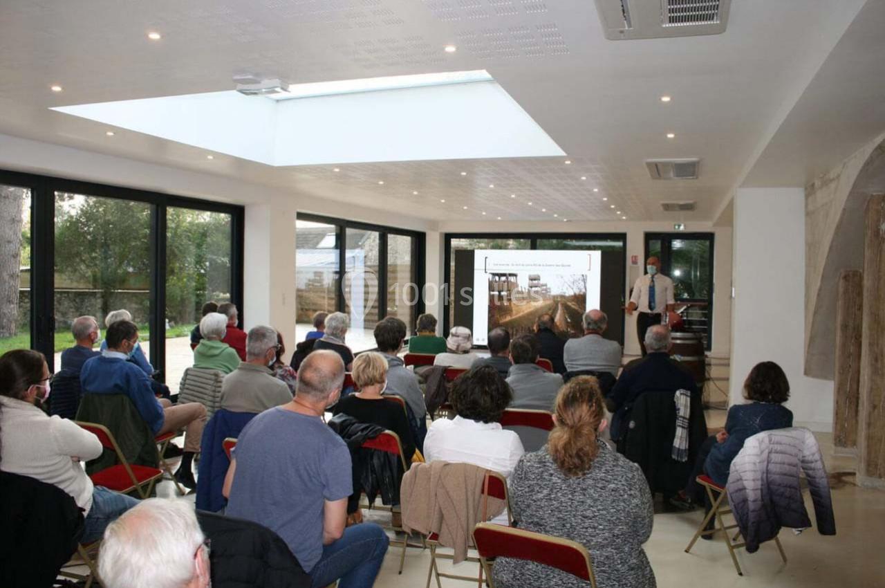 Un groupe de personnes assises assiste à une présentation avec un écran projetant une image dans une salle lumineuse.